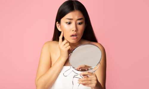 Pretty girl holding mirror, touching and worrying about her face, pink background